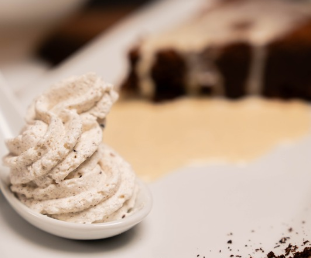 Cuillère de chantilly à la vanille de Madagascar parsemée de grains noirs, posée sur une assiette de dessert gastronomique