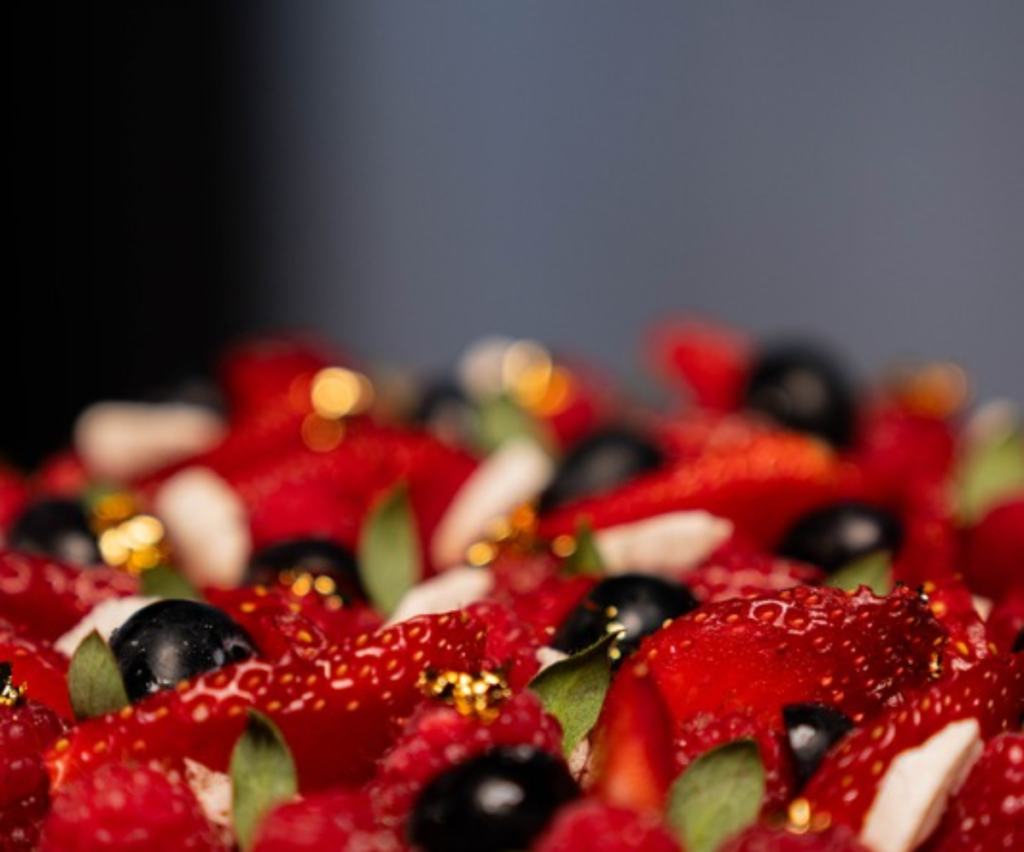 Tarte pâtissière aux fraises, framboises, myrtilles et feuilles de menthe, avec éléments dorés, sur fond sombre