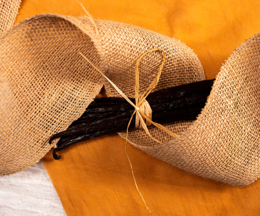 Fagot de gousses de vanille noire de Madagascar attachées avec une ficelle naturelle, posées sur une toile de jute orange